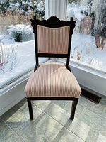 Front view of the carved wood accent chair with pink and white striped upholstery on the seat and backrest.