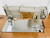 Close-up front and side view of the Singer sewing machine mounted in the table, showing control dials and labels.