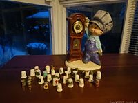 Front view of boy figurine in chef's hat beside wooden grandfather clock and assortment of collectible thimbles on a table.