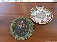Photo showing two decorative plates side by side on wooden surface: Mason's Ironstone Buckingham Palace commemorative plate and religious art plate with woman and child.