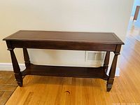 Front view of dark wood console table showing rectangular top and lower shelf with tapered legs.