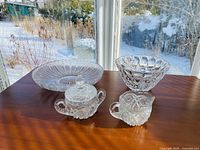 All four pieces of crystal serving ware together on wooden surface in natural light, showing clear glass and intricate cut patterns