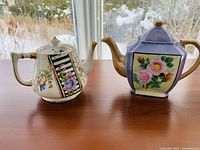 Front view of both decorative floral teapots showing colors and floral designs.