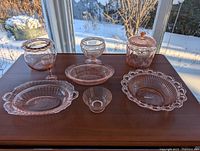 Wide angle showing all seven rose coloured Depression glass pieces on a wooden surface in natural light.