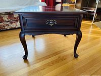 Front view of the Gibbard end table showing the drawer with brass handle and carved legs.