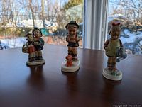 Front view of three Hummel figurines arranged on a table: girl watering flower, boy and girl with picnic basket, boy with rabbit.
