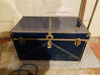 Front view of blue metal trunk showing locking latch and corner protectors