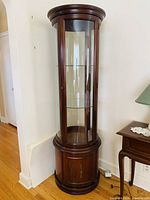 Front and side view of the tall round curio cabinet with glass door and wood lower cabinet.