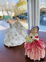 Both porcelain figurines side by side on a wooden table in natural light, showing overall appearance.