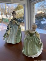 Front view showing the two Royal Doulton figurines on table with window background.