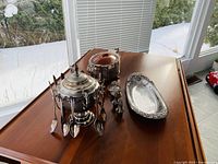 Photo showing silver serving dish with multiple spoons attached, a silver platter, two wine stoppers, and another covered silver serving dish.