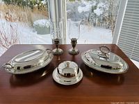 Front view of the silver serving set including two covered serving dishes, covered butter dish, and two candle holders with etched glass shades.