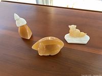 Three stone carved figurines displayed on a wooden surface: a woman, a rabbit, and a fox on a white base.