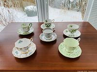 Top view of all 6 teacups seated on matching saucers arranged on wooden table near window with snowy outdoor background