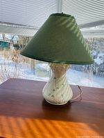 Full side view of vintage Belleek porcelain table lamp with green shade displayed on wooden surface in daylight, showing embossed shamrock and daisy flower details on cream base.