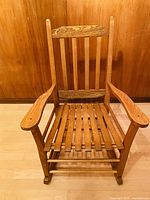 Front view of wooden rocking chair showing slatted backrest and seat and wide armrests.