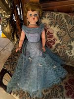 Full body image of the vintage 1950s Darling Debbie doll seated, dressed in a layered blue tulle and lace dress with some wear visible on the skirt.