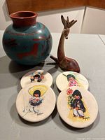 Photo showing vase, deer figurine, and four DeGrazia coasters grouped together on table.
