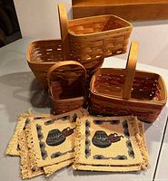 Photo shows four woven Longaberger baskets in a variety of sizes, arranged with southwest style woven mats featuring a pot and flame design and fringe edges in front.
