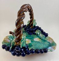 Front angled view of the Majolica leaf-shaped bowl with twisted handle and grape clusters.