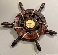 Full view of vintage burnt wood ships wheel with rope and a thermometer inset in the center.
