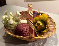 Woven wicker basket with silk fabric vegetables inside including cabbage and flower-like vegetable.