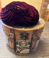 Top view of the round wooden hat train carry-on case with vintage absynthe label and deep magenta ruched velvet hat placed on top.