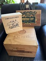 Set of four wooden boxes and a WINE decorative sign arranged on a black couch showing front branding of each box for display and storage use.