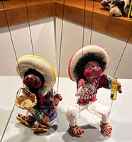 Two vintage Mexican puppet dancers displayed on a table corner with strings attached for manipulation