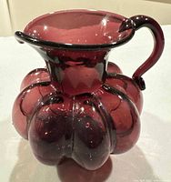 Front angled view of amethyst melon shaped glass jug with handle and flared rim.
