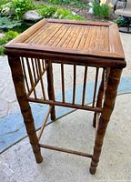 Side angle view of the vintage burnt bamboo/rattan plant stand showing the slatted sides and top with square shape and tapered legs.