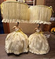 Pair of vintage porcelain boudoir lady lamps on a table, showing full lace skirts and fabric lampshades with lace trim and ribbon ties.