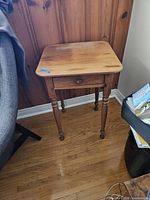Front view of pine side table showing smooth wood top, turned legs, and single drawer closed.