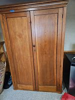 Front view of closed armoire showing two-panel pine doors with keyhole and knob handles, crown molding.
