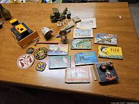 Overview photo showing a variety of vintage childhood items including toy military vehicles, patches, flashcards, and games arranged on a wooden table.