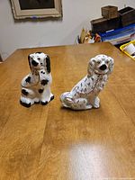 Pair of vintage Staffordshire porcelain dog figurines on wooden table, showing front views and detailing