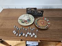 Overview of all items on wooden table, including decorative plates, carved bookends, and souvenir spoons laid in front.
