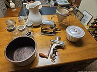 Overview of all 11 vintage kitchen items including pitcher, jars, bowl, grinders, and other implements arranged on wooden table.