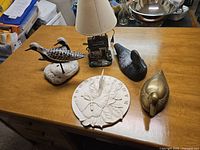 Full view of all five folk art pieces on table: three bird decoys, house lamp, decorative clock.