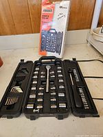 Photo showing entire open tool set with sockets, hex keys, ratchet driver, screwdriver handle and bits neatly organized in carrying case with original box behind.