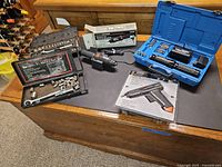 View of multiple electric screwdrivers, socket sets in cases, and boxed glue tool arranged on wooden surface.