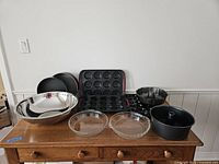 Overview of all 10 bakeware pieces on wooden table including mixing bowl, pie dishes, cake pans, and mini muffin trays.