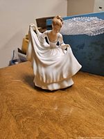 Porcelain figurine showing woman in white dress bowing, holding skirt sides.
