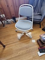 Full view of computer desk chair showing light gray cushioned seat and back with white metal frame and wooden floor background
