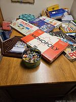 Photo of a wooden table with various classic board games and toys including Monopoly Canadian Edition and a wooden marble solitaire board with marbles.