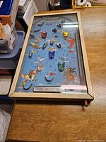 Full view of the rectangular antique electric tabletop pinball game in wooden frame with glass cover on a wood surface.