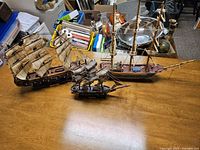 Three wooden model ships of varying sizes displayed on a wooden table, showing overall scale and detail.