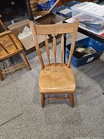 Front view of the 19th century solid wood plank chair showing the seat, legs, and slat backrest.