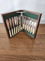 Overview photo of the fish service set displaying six knives and six forks in the open walnut box, secured with green felt lining and fabric straps.