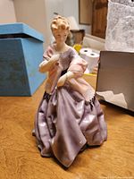 Side view of one porcelain figurine in purple dress with pink shawl, showing detailed craftsmanship and color.